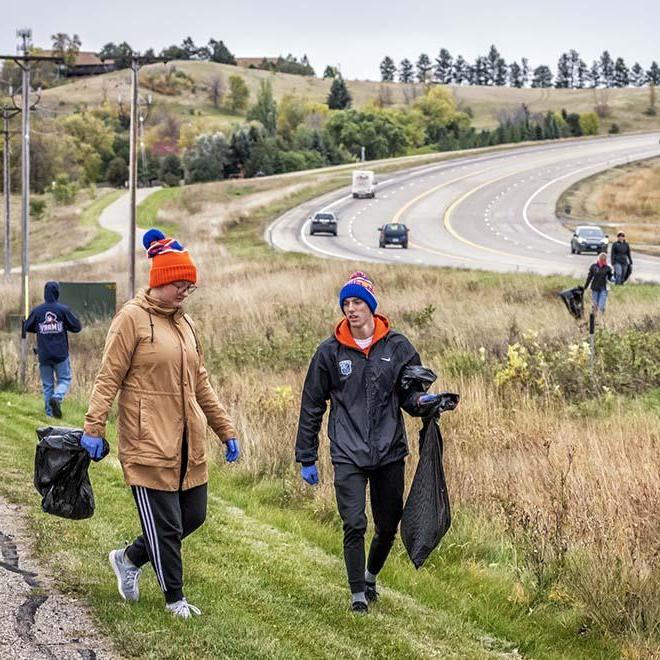 Two Mary students carrying trash bags alongside the highway